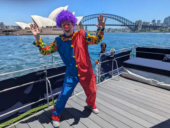 A colleague in a full clown costume on a boat, the Sydney Harbour Bridge behind.