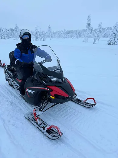 A colleague riding a snowmobile across an open snowfield.