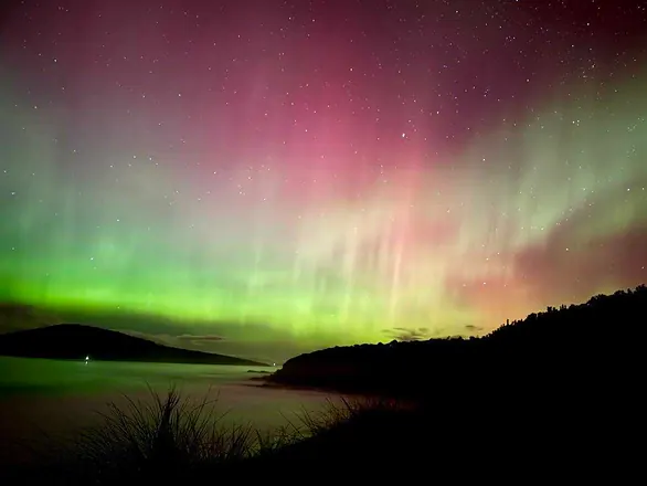 The northern lights over a dark coastline.