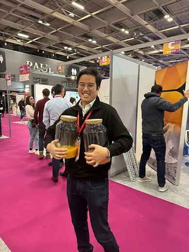 A colleague carrying two drinks down the pink carpet of a trade show floor.