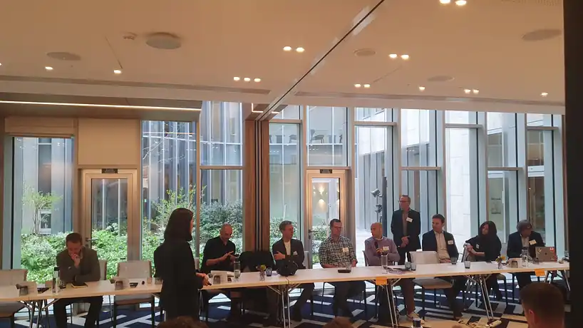 A meeting under way around a long table in a glass-walled office.