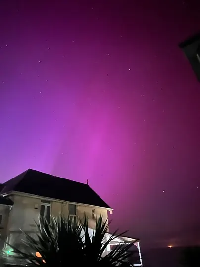 A magenta aurora filling the sky above a house.