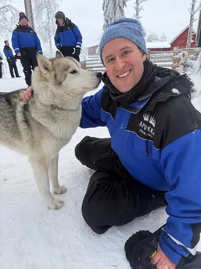 A colleague crouched in the snow beside a husky.