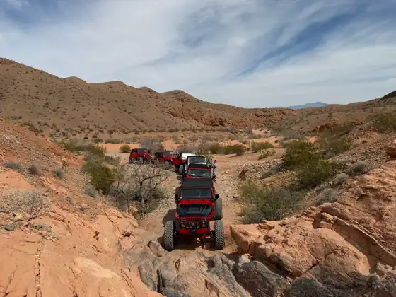 A line of off-road vehicles picking through a red rock canyon.
