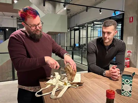 Two colleagues at a table in the office, unpacking a tote bag.