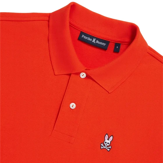 An orange-red Psycho Bunny polo shirt with the bunny and crossbones mark on the chest