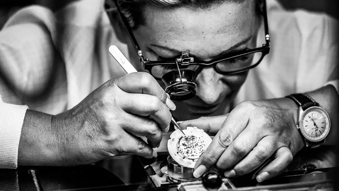 A Breitling watchmaker examining a movement through a loupe.