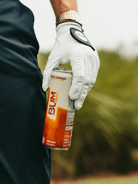 A golfer in a white glove holding a can of BUM Energy iced tea lemonade.